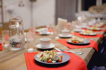 Wooden table with separated plates with salad, tea mugs and glass glasses. Concept dinner, tea party.