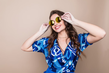 Beautiful cheerful summer young woman in sunglasses standing over a color background