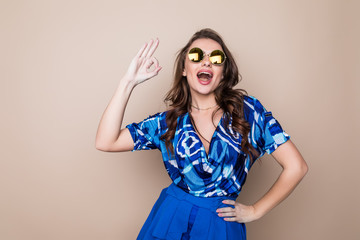 Beautiful cheerful summer young woman in sunglasses standing over a color background