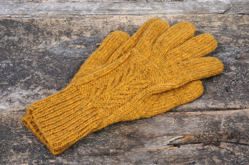 Yellow handmade gloves on a wooden background. Front view.