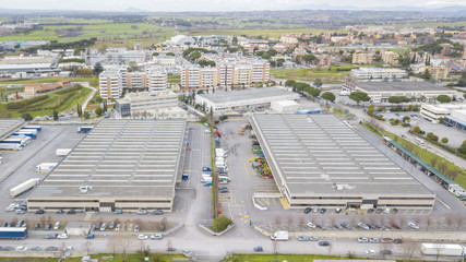 Aerial view of an industrial area of a large Italian city with warehouses, warehouses, offices and buildings. Among the asphalt roads beyond the cars, vans and trucks there are trees.