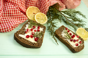 Black bread with grenades berries on turquoise wooden background. Christmas food, Christmas decorations with lemon, juniper, branch, red berries