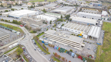 Aerial view of an industrial area of a large Italian city with warehouses, warehouses, offices and buildings. Among the asphalt roads beyond the cars, vans and trucks there are trees.