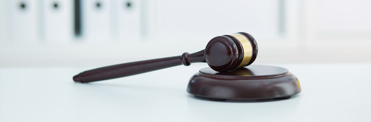 Brown wooden judge gavel lies on a wooden plate on white table.