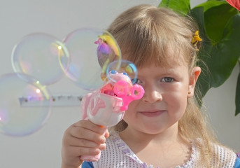 little girl blowing bubbles on the balcony in the sun