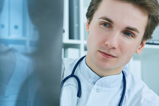 Close up portrait of young male doctor holding x-ray or roentgen image.