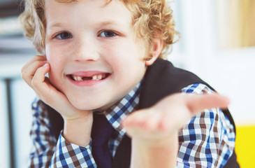 Litle caucasian boy holds a dropped milk tooth between his fingers and laughs looking into the camera.