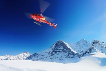 Foto op Plexiglas Rode helikopter die in de winter de Zwitserse Alpenberg Mannlichen vliegt © Roman Babakin