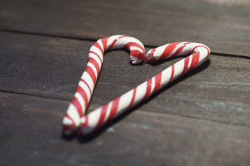 Red and white candy canes forming a heart on a background of dark wooden planks. Close up. Christmas photo 