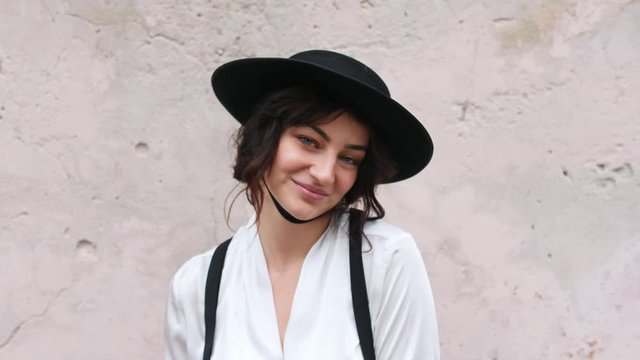 Close-up of a girl in a hat is standing by the wall and posing for the camera.