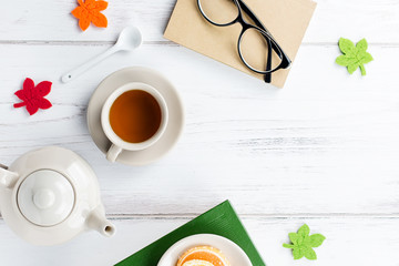 Book, cup of tea, teapot, sweets and eyeglasses, flat lay. Cozy background, reading concept. Copy space