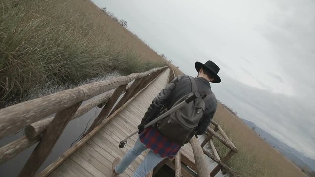 Ragazzo sta camminando su un piccolo ponte di legno in una palude mentre riprende con la sua telecamera