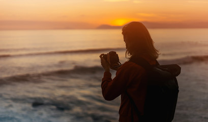 Hipster hiker tourist making photo of seascape sunset on camera on background sea, photographer on ocean horizon, panoramic sunrise, traveler blogger relax holiday concept, sunlight in trip vacation