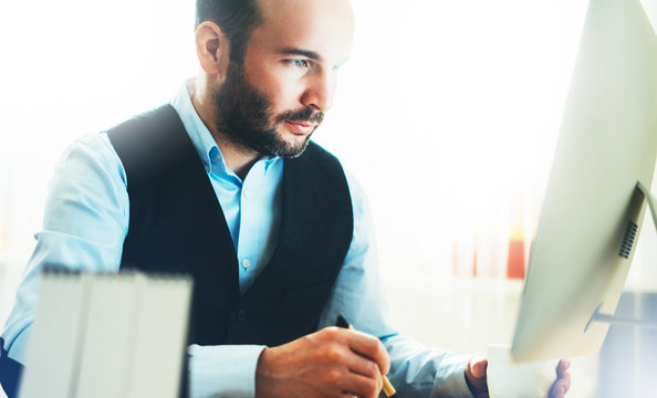 Bearded young businessman working on modern office. Consultant man thinking looking in monitor computer. Manager typing on keyboard in coworking workplace