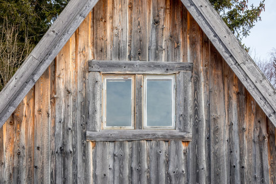 Front view of two windows on a weathered and aged log cabin.
