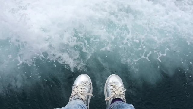 Woman's feet in silver snickers infront of the sea.