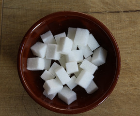 Stone bowl with sugar cubes in kitchen on wooden background