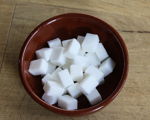 Stone bowl with sugar cubes in kitchen on wooden background