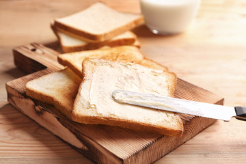 Wooden board with tasty toasted bread and butter on table