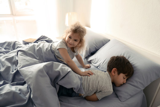 Cute Little Girl Waking Up Her Brother On Bed At Home