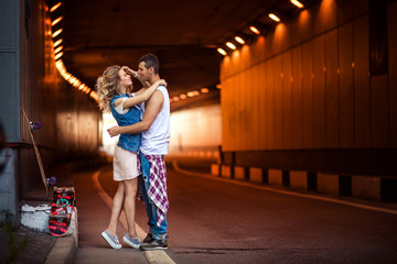 Naklejka na ściany i meble Portrait of female and male skaters embrace passionately, going to kiss, stand against tunnel background, recreat after active skateboarding in open air. People, relations and sporty lifestyle.