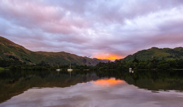 A lake with boats giving reflection to a red clouded sunset