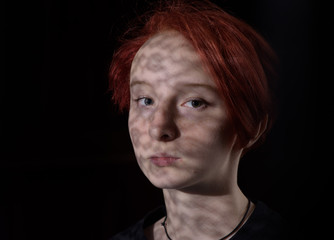 red-haired girl stands at the window with a shade of curtains on her face