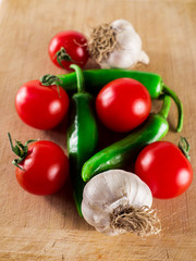 Cherry tomatoes, green hot peppers and garlic over wooden table background.