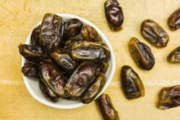 Dried dates in a white bowl and spread out on a wooden board.