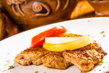 Grilled pork steak with onion rings and tomato slice on white plate
