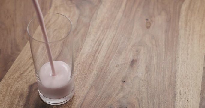 Slow motion por strawberry yogurt into glass on wood table