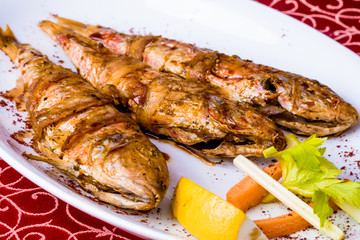 Grilled surmullet fish wrapped in bacon on white plate. Close-up