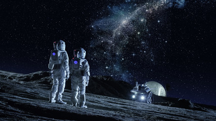 Two Astronauts in Space Suits Stand on the Planet and Looking at the The Milky Way Galaxy. In the Background Lunar Base with Geodesic Dome. Moon Colonization and Space Travel Concept. - obrazy, fototapety, plakaty