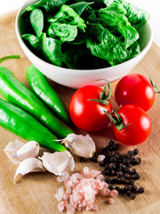 Pink cristal salt, black pepper,cherry tomatoes, green hot peppers, spinach and garlic over wooden table background.