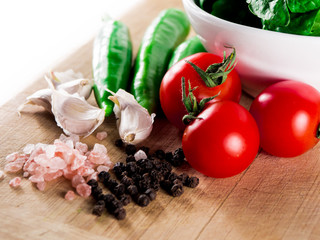 Pink cristal salt, black pepper,cherry tomatoes, green hot peppers, spinach and garlic over wooden table background.