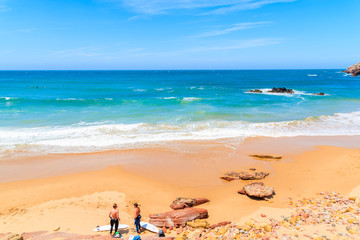 Fototapeta na wymiar PRAIA DO AMADO BEACH, PORTUGAL - MAY 15, 2015: Surfers relaxing on Praia do Amado beach with ocean waves hitting shore. Algarve region is popular holiday destination in southern Europe.