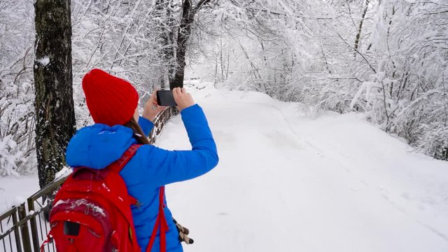 Young woman uses a smartphone for make a photos of a beautiful winter snow-covered landscape