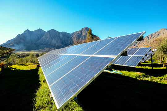 Solar panels with photovoltaic  modules for renewable energy with blue sky and mountains in the back round set in a countryside meadow 