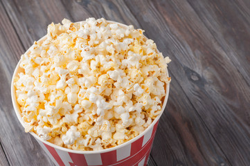 Popcorn in a striped bucket (red and white box) isolated on grey wooden table (background). Top view. Selective focus. Copy space. Nobody.