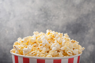 Popcorn in a striped bucket (red and white box) isolated on grey wooden table (background). Selective focus. Copy space. Nobody. Front view.