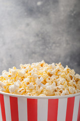 Popcorn in a striped bucket (red and white box) isolated on grey wooden table (background). Selective focus. Copy space. Nobody. Front view.