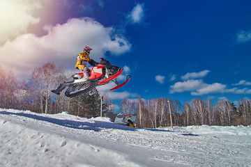 Sports race snowmobiles. Snowmobile in  high jump above track. Sportsman on snowmobile. Winter competition, sunny day, blue sky. Copy space.