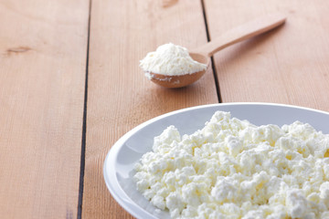 Cheese, fresh cottage cheese in a white plate, wooden spoon, curd on a wooden background, sour cream in a wooden spoon, dairy products on a natural background, retro style, minimalism