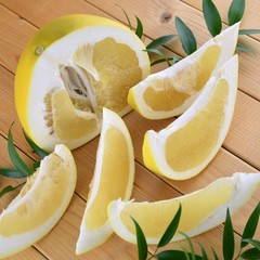 A half of pomelo and it's cut pieces on wooden background with green leafs, cut pomelo close up