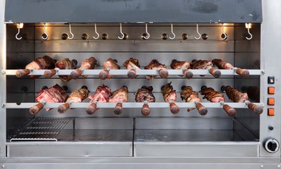 Professional rotisserie electric barbecue. Brazilian skewers are on spit, some cooked and others not