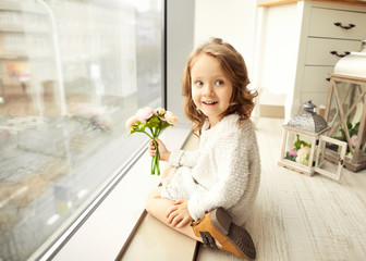 .A little girl with a bouquet of flowers on her mother's day sits at the window and laughs at her mother, gives a bouquet of flowers.