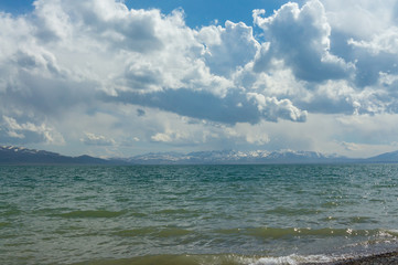 Elegant view of the mountain lake Son Kul with curly clouds and blue sky