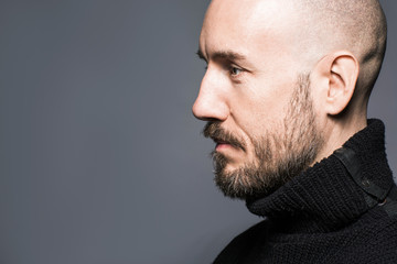 Fototapeta premium Fashion Portrait of a 40-year-old man standing over a light gray background in a black sweater. Close up. Classic style. Bald shaved head. Copy-space. Studio shot