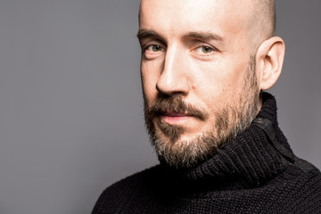 Fashion Portrait of a 40-year-old man standing over a light gray background in a black sweater. Close up. Classic style. Bald shaved head. Copy-space. Studio shot