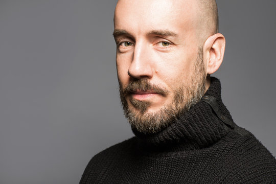 Fashion Portrait of a 40-year-old man standing over a light gray background in a black sweater. Close up. Classic style. Bald shaved head. Copy-space. Studio shot.